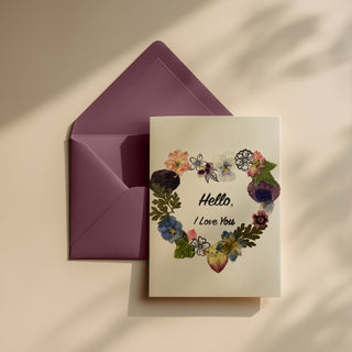 Hand made greeting card with floral design made using real pressed flowers and 'Hello, I Love You' text on a beige background