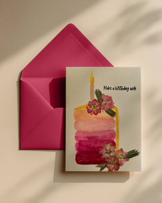 Greeting card with a watercolor cake slice in shades of peach and pressed flowers decorating it, matched with a bright coral envelope 